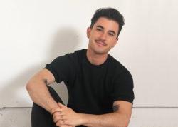 Headshot photograph of a seated man wearing a black shirt, black pants.