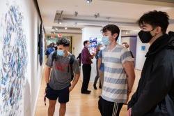 Three students wearing face masks look at a piece of art on the wall.