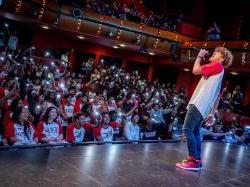 Student stands on stage and sings into a microphone in front of a large audience.