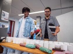 Two students play the thongophone, striking different size pipes with rubber thong like sandals.