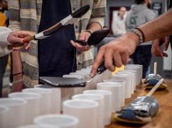 Hands holding rubber sandals taped on to spatulas strike white pipes of different sizes.