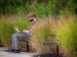 Male sitting outside on a bench, wearing a mask