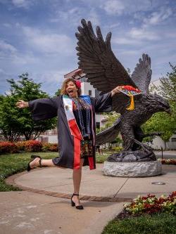 A graduate celebrates in front of the Red Hawk statue.