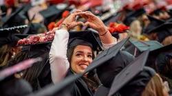 A graduate smiles and holds up their hands in the shape of a heart