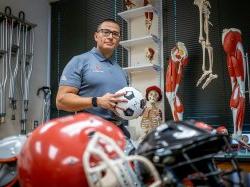 Luis Torres holds a soccer ball in a classroom filled with sports equipment.