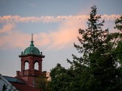 College Hall bell tower with a evergreen tree to the left and a slightly pinkish evening sky with clouds