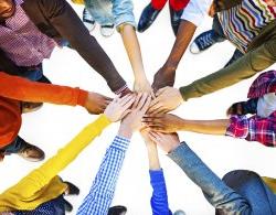 Photo of about 10 individuals in a circle with their hands together symbolizing teamwork.