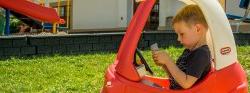 Image of a child sitting in a play car dialing on a play phone.