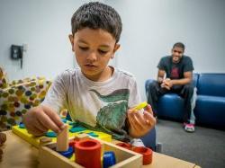 photo of young boy playing with blocks in foreground and an adult blurred in the background