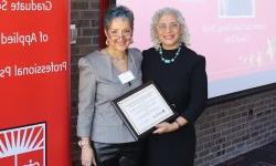 two people stand smiling, one is holding a certificate