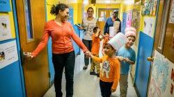 Photo of teacher with young students in a school hallway.