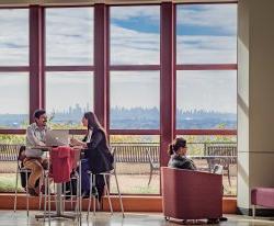 Three students sitting by large window in CELS building overlooking the NY skyline.